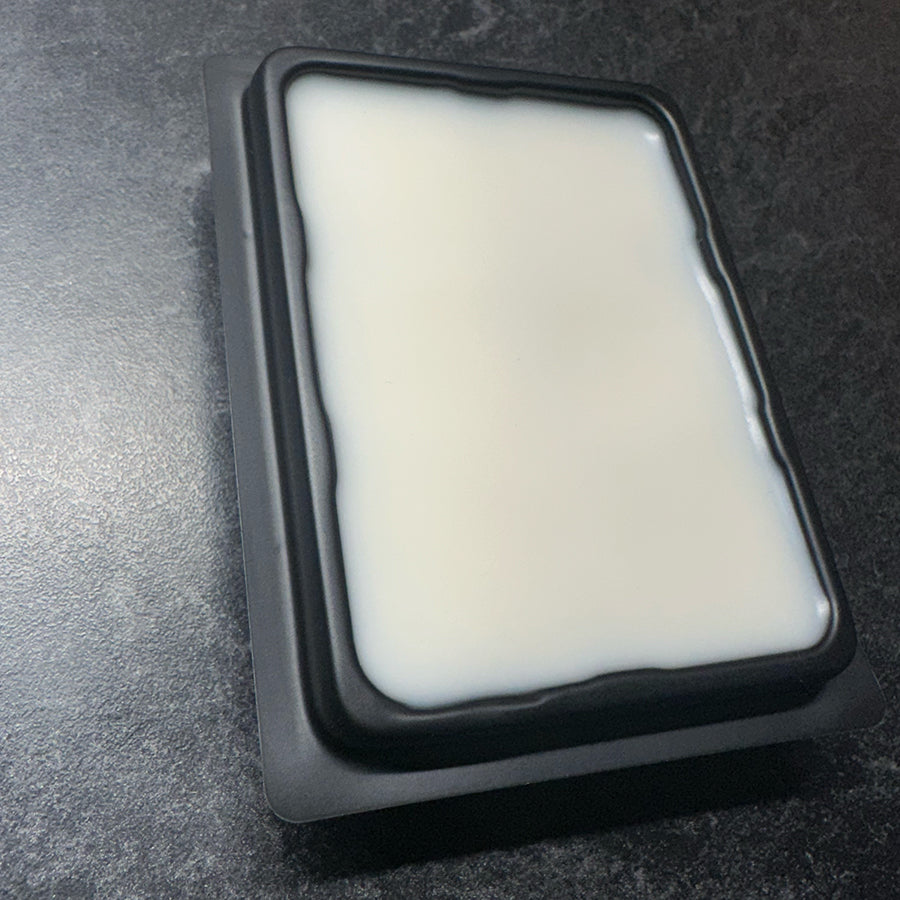 A black moody background with a black rectangular wax melt container holding an off white wax.